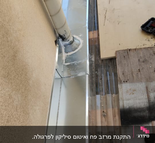 תעלת ניקוז מתכתית ליד קיר עם צינור פלסטיק
